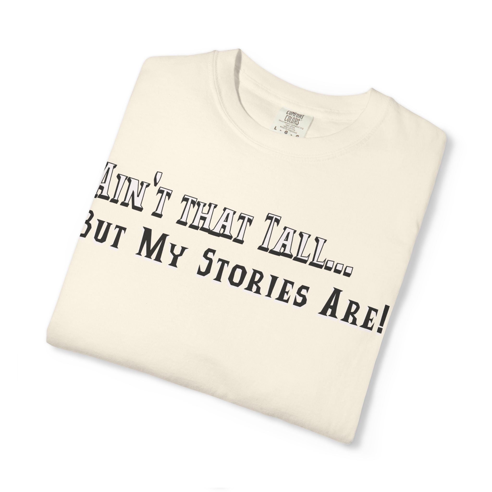 Folded t-shirt with text 'Ain't that tall... but my stories are!' on a white background