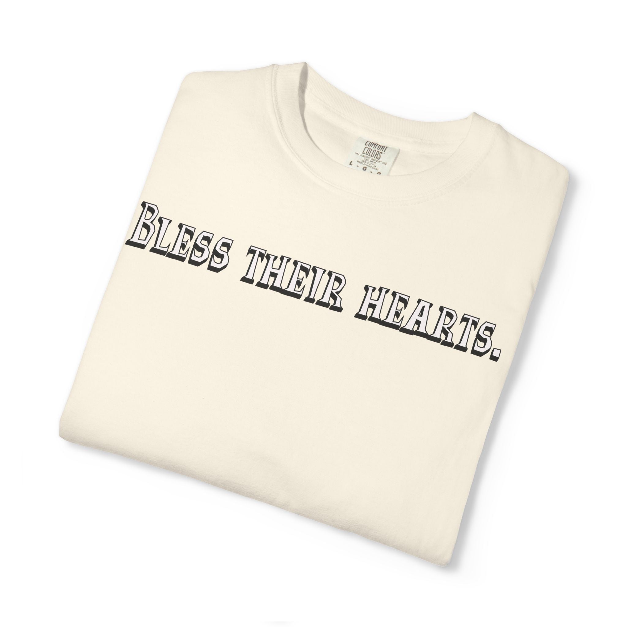 Folded cream-colored t-shirt with 'Bless their hearts.' text on a white background